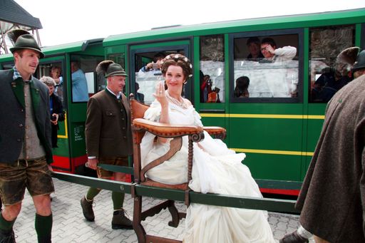 Vorschau Bild von Kaiserliche Bergtour wie vor dem Bau der SchafbergBahn. Sisi Darstellerin Maya Hakvoort wurde von vier Sesselträgern zu ihrem glanzvollen Gastauftritt auf der Schafbergspitze getragen. (Auf einem originalen Stuhl von Erzherzogin Sophie.) Im Geleit politische Prominenz von Salzburg und Oberösterreich.