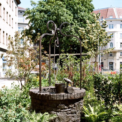 Mit der Installation eines aus Bronze gegossenen Ziehbrunnenobjekts inmitten eines scheinbar privaten Gartens im öffentlichen Raum setzt die Künstlerin Inés Lombardi den Zimmermannplatz in Relation zu seinem längst vergangenen Vorstadtleben.