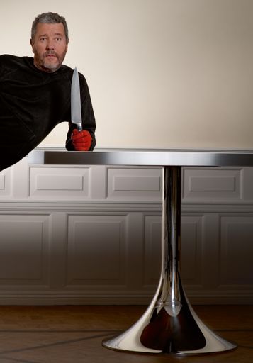 Vorschau Bild von "STARCK BY WARENDORF" Philippe Starck mit rotem Handschuh mit Messer auf verchromten Trompetenfußtisch