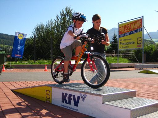 Vorschau Bild von Fahrradlehrer der Mobilen Radfahrschule, Helmi und die Mitarbeiter des KfV haben beim Training ein wachsames Auge auf die Fahrradsicherheit der Kleinen.