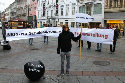Bei einer Straßenaktion zeigten die Jugendorganisation SJ, FSG-Jugend, AKS, IKS und VSStÖ ihren Unmut über die Schuldenbremse am Linzer Taubenmarkt. Gebremst von einer überdimensionierten Fußfessel samt Kugel zeigten die Vertreter_innen der Jugendorganisationen, was die Schuldenbremse für die Zukunft Österreichs bedeutet: eine Bremse auf dem Weg zu einer sozial gerechteren Zukunft.