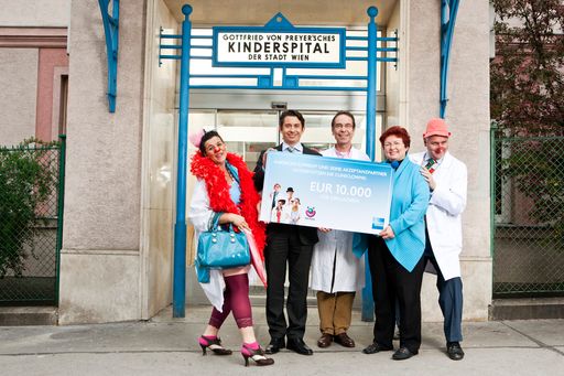  Lachende Scheckübergabe an CliniClowns: Ragnar Graetz, Direktor Vertragspartnerservice bei American Express, Günther Bernert, Abteilungsvorstand des Preyer'schen Kinderspitals und Liane Steiner, Generalsekretärin der CliniClowns (v.l.n.r.), flankiert von den Spitalsclowns.