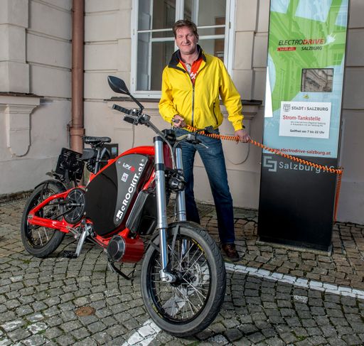 Vorschau Bild von E-Biker Hannes Valenta beim "Auftanken" des eRockits an der
Stromtankstelle im Salzburger Schloss Mirabell.