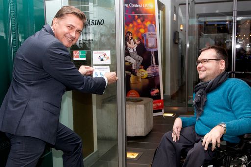 Vorschau Bild von Casino Direktor Reinhard Deiring beim Anbringen der
Auszeichnung für Barrierefreiheit seines Casinos und Restaurants.