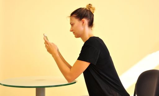 Vorschau Bild von Die beste Variante bei der Smartphonenutzung: Mit
den Ellenbögen stützt sich die Userin an einem Tisch ab