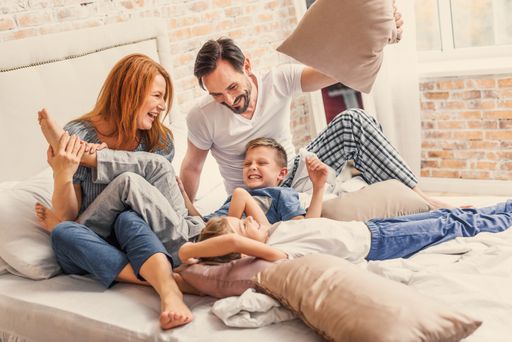  Our happy family. joyful parents spending time with
their smiling children while playing with pillows in bed