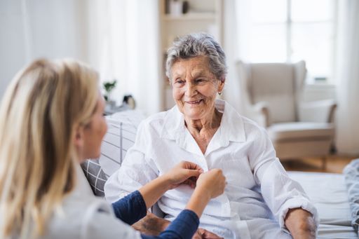  A young health visitor helping a happy sick senior
woman sitting on bed at home.