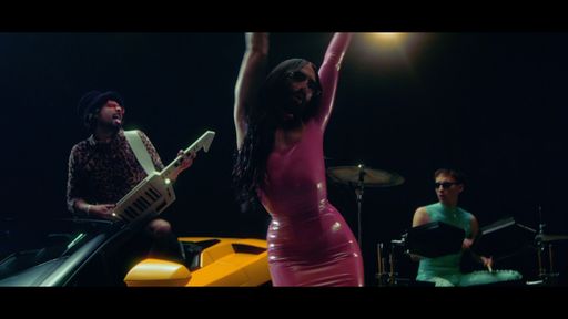 Vorschau Bild von Conchita Wurst performt mit Martin Zerza (keytar)
und Lukas Klement (drums) in einem rosa Latexminikleid im Musikvideo
zu CAR (IDHLARGT)