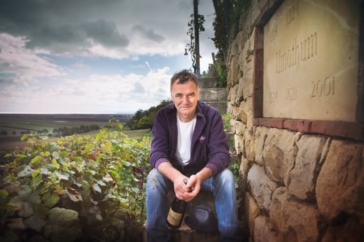 Josef Umathum sitzt im Weingarten vor Steinmauer