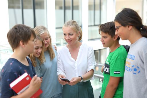  Lehrerin inmitten einer Schülergruppe hält eine
Smartphone in der Hand