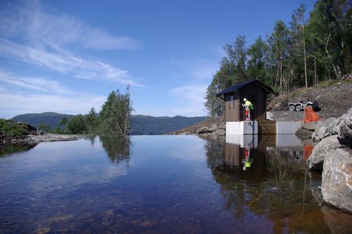 Vorschau Bild von enso hydro - Wasserkraftwerk Norwegen Wasserfassung
des Kraftwerkes Borgåna am Boknafjorden. Die Wasserfassung besteht
aus einer niedrigen natürlichen Schwelle mit einer Seitenentnahme
des Triebwassers für die Druckrohrleitung. Wie bei allen Kraftwerken
sind die baulichen Eingriffe in die Natur minimal und als
Kraftwerksbauten kaum sichtbar, da ideal an die Umgebung angepasst.
Der Druckrohleitungsanschluss, der Rechen und das zugehörige
Verschlussorgan sind in der kleinen Hütte untergebracht.