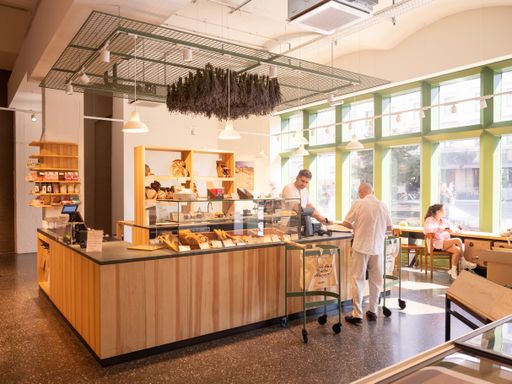 Vorschau Bild von Im Bereich der beiden Kassen können Kund:innen
frischen Kaffee trinken und auf einem der Sitzplätze bei einer
Zeitung genießen.
