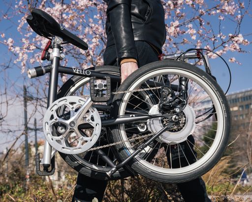  Gefaltetes VELLO Bike+ GEARS Faltrad vor einer
frühlingshaften Outdoorkulisse in der Wiener Innenstadt.