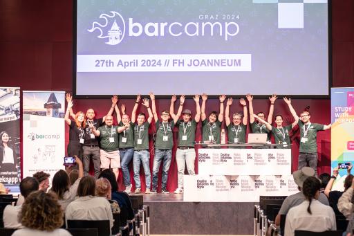 Vorschau Bild von Das Organisationsteam des Barcamp Graz 2023 auf der
Bühne mit erhobenen Händen zur Feier am Ende der Abschlusssession,
vor einem Hintergrund mit den Details zur 2024 Veranstaltung.