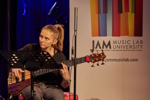 Vorschau Bild von Nina Feldgrill spielt live mit Bass, im Hintergrund
ein Roll-Up der JAM MUSIC LAB Privatuniversität