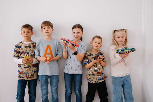  Fünf Kinder stehen nebeneinander und halten verschiedene
Spielzeug-Verkehrsmittel in ihren Händen.
