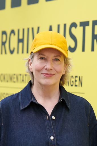 Abgebildet ist Marlene Ropac mit einer gelben Schirmkappe vor
einem gelben Transparent des Filmarchiv Austria.
