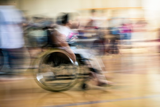 Vorschau Bild von Das Bild ist vor lauter Bewegung ganz verschwommen. Ein Kind
fährt in einem Rollstuhl sehr schnell an der Kamera vorbei.