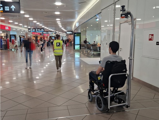 im Flughafen, autonomer Rollstuhl für Passagiere mit
eingeschränkter Mobilität folgt einer Assistenzperson, die einen Tag
auf der Warnweste hat