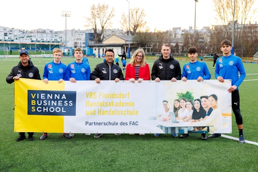 Die Direktorin der VBS Floridsdorf, Astrid Holzer, mit U16
Trainer Lukas Moser und Spielern bei der Übergabe der Bandenwerbung
.am FAC Platz