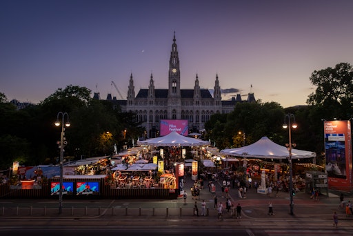 Eröffnungsabend des 35. Filmfestivals auf dem Wiener
Rathausplatz: Blick über die Ringstraße und den Gastronomiebereich
mit 28 teilnehmenden Betrieben auf die imposante Filmleinwand und
das festlich beleuchtete Rathaus kurz vor Filmbeginn.
