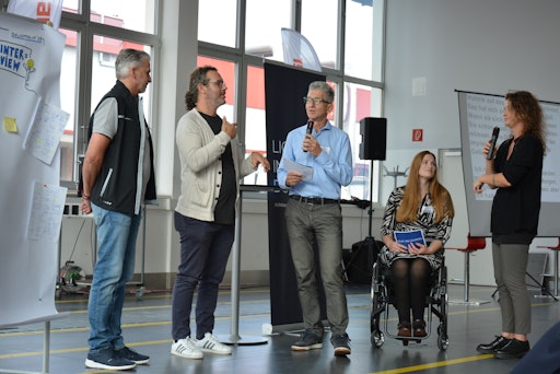 Zwei Mitarbeiter von Rosenbauer International im Gespräch mit den
zwei Moderatorinnen beim dritten LICHT INS DUNKEL-Dialogforum zum
Thema inklusive Arbeitswelt. Eine ÖGS-Dolmetscherin übersetzt die
Wortmeldung einer der beiden Mitarbeiter. Im Hintergrund sieht man
die Live-Schriftdolmetschung.