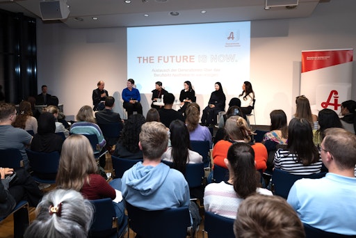 Vorschau Bild von Podiumsteilnehmer im Hintergrund und Publikum im Vordergrund