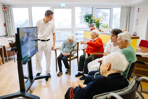 Vorschau Bild von Eine Gruppe von Bewohnerinnen im Pflegehaus sitzen um den
digitalen Aktivtisch und spielen zusammen mit den Zivildienern ein
Quiz.