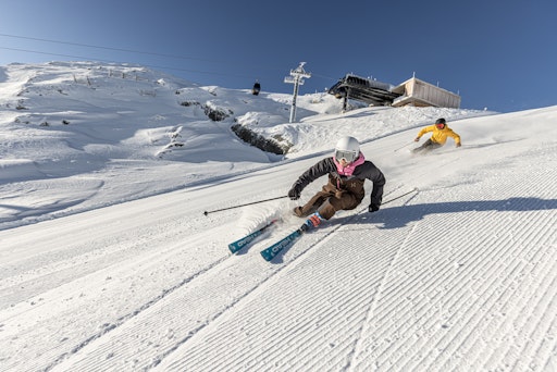 zwei Skifahrer carven auf einer frischpräparierten Piste bei
blauem Himmel