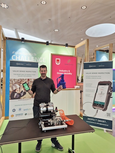 Vorschau Bild von Adam Bezeczky, Global Sales and Partnership Manager, präsentiert
das Senseven "Valve Sense"-Inspektionsgerät beim Finale der
#glaubandich Challenge den BesucherInnen.