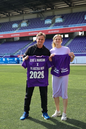 Eine Frau und ein Mann in einem Fußballstadion mit Fußballdressen
in der Hand