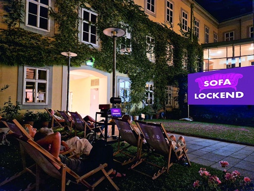 Vorschau Bild von Eine Leinwand im Innenhof des Möbelmuseums in Wien sowie
Liegestühle mit Zuschauerinnen und Zuschauern