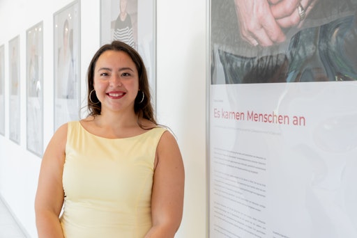 Soziologin Dilara Gündüz neben dem Ausstellungsplakat „Es kamen
Menschen an“. Die Aufnahme entstand im Ausstellungsbereich der
Pädagogischen Hochschule Wien.
