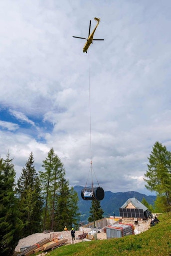 Vorschau Bild von Da die Hütte nicht mit schweren Fahrzeugen erreichbar ist,
mussten Baumaterialien, Maschinen und technische Anlagen nahezu
vollständig per Hubschrauber transportiert werden. Große Bauteile
wie Wasserbehälter oder Elemente der Pflanzenkläranlage wurden aus
der Luft angeliefert und anschließend händisch eingebaut.