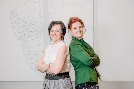 Vorschau Bild von Sylvia Loidolt und Susanne Haubenhofer stehen mit verschränkten
Armen Rücken an Rücken.
