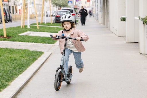 Vorschau Bild von Ein junges Mädchen fährt mit ihrem Roller auf einem Gehweg. Sie
trägt dabei einen Schutzhelm.