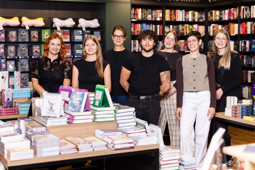 Mitarbeiterinnen und Mitarbeiter der neuen Thalia Buchhandlung im Sillpark stehen gemeinsam an einem Tisch mit Geschenkartikeln und Kalendern.